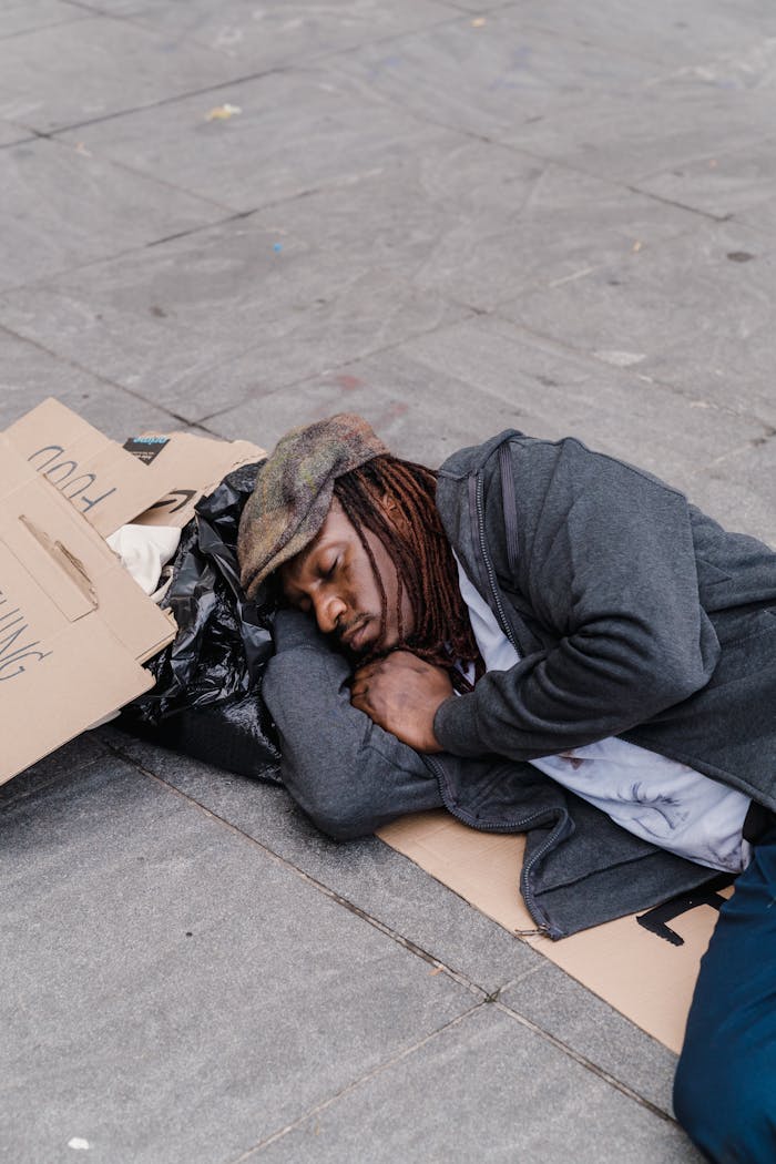 who-we-are A homeless man sleeping on the street with cardboard signs and belongings.